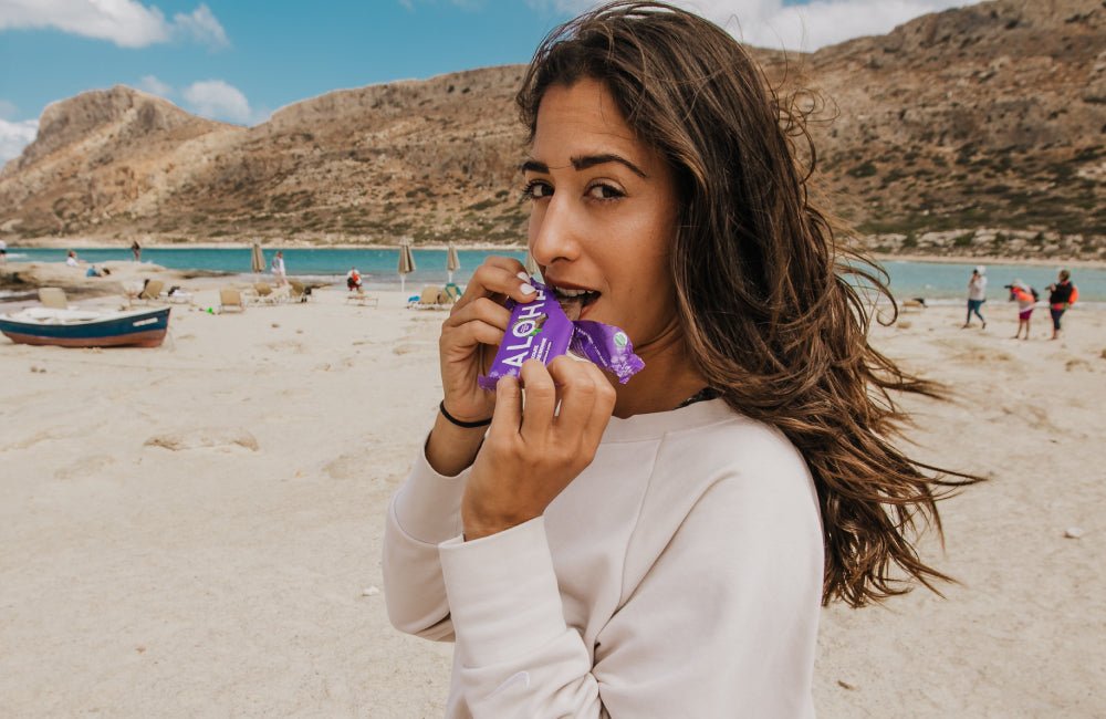 Woman enjoying ALOHA chocolate brownie protein bar on the beach